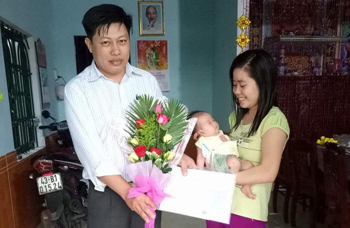 An official of the Hoa Nhon administration hands flowers and a birth certificate to a resident and her baby at their home. Photo: Tuoi Tre