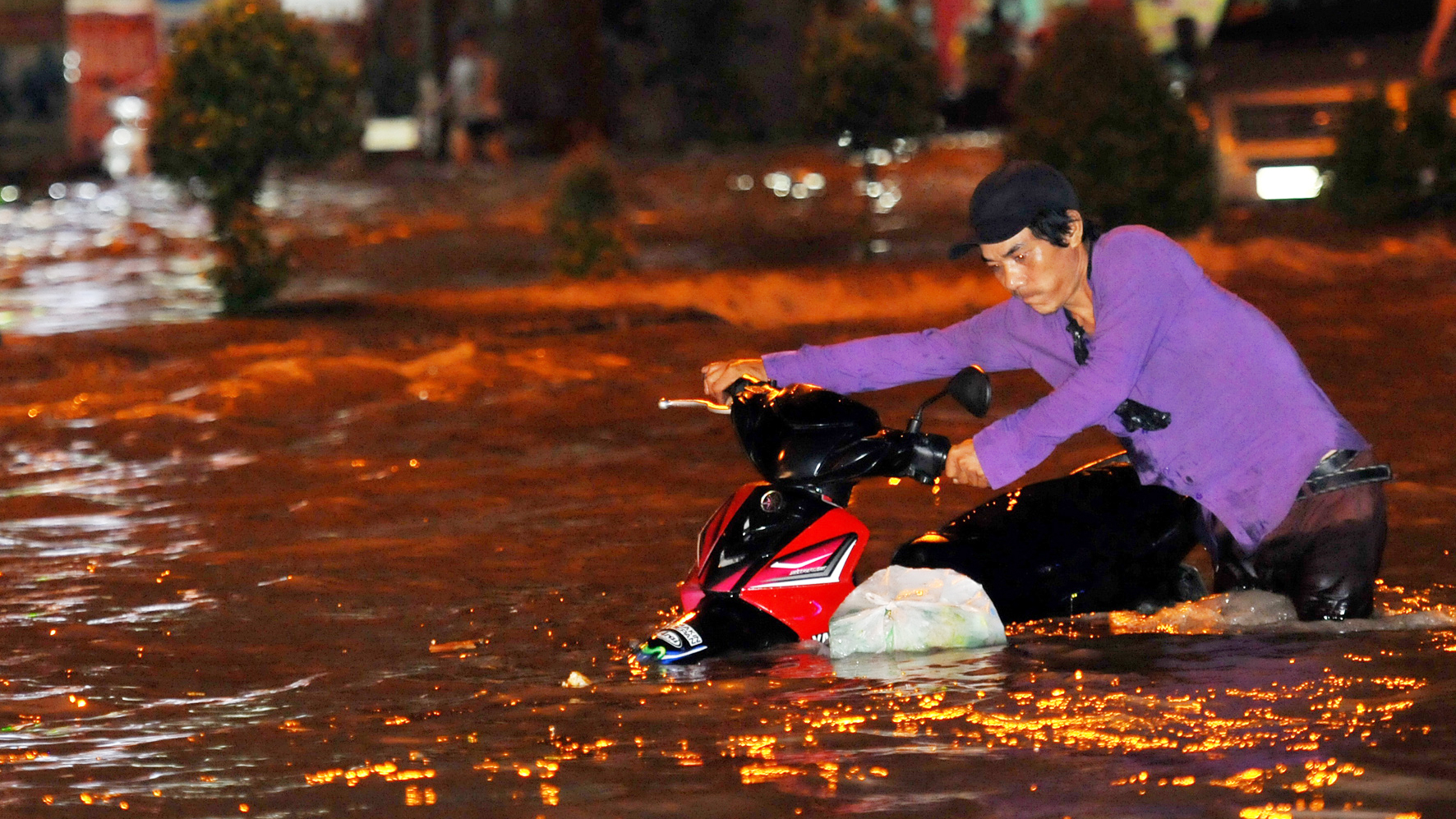 A man pushes his motorbike through the floodwater.