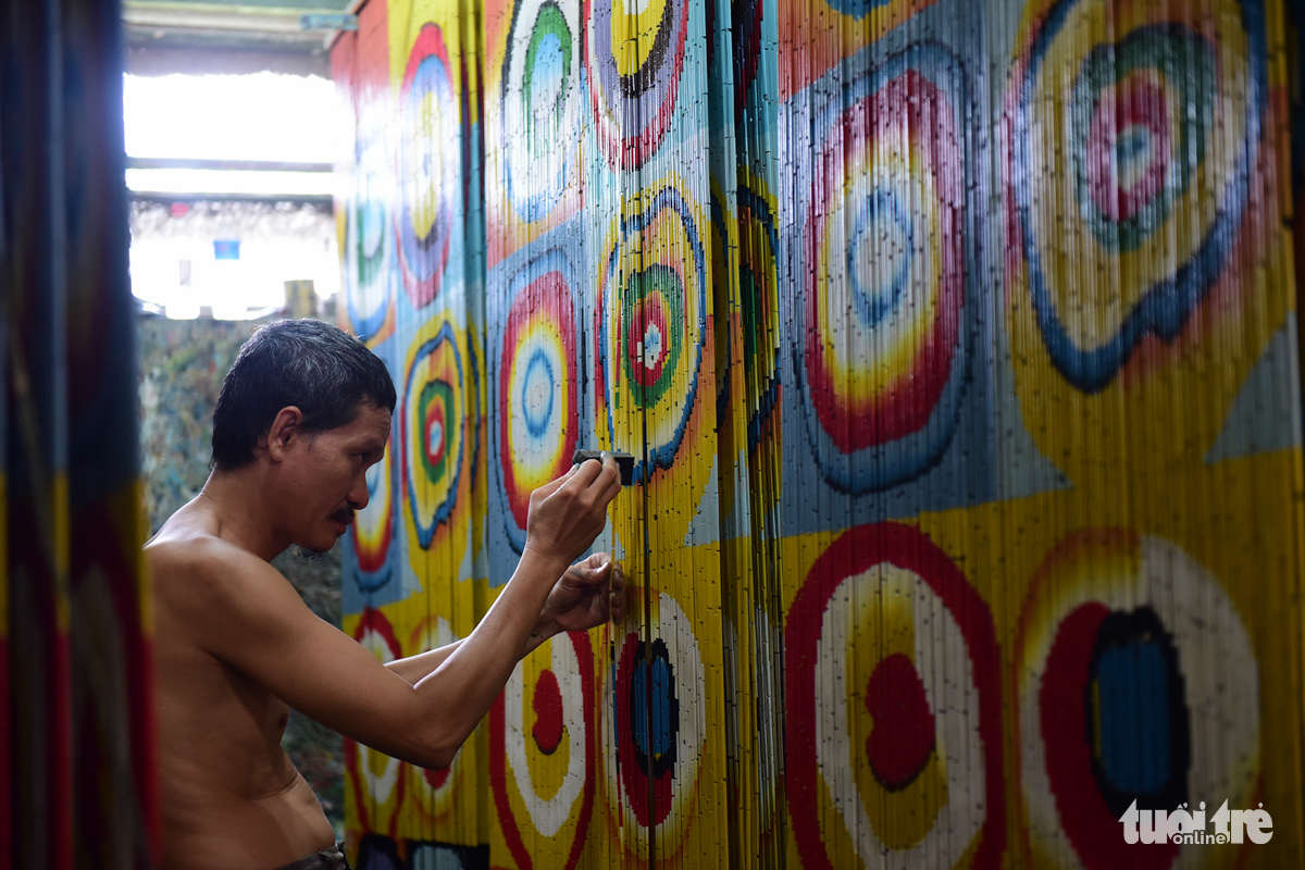 An artisan carefully hand-paints tiny pieces on a bamboo curtain at the workshop of Nguyen Van Ben. Photo: Tuoi Tre
