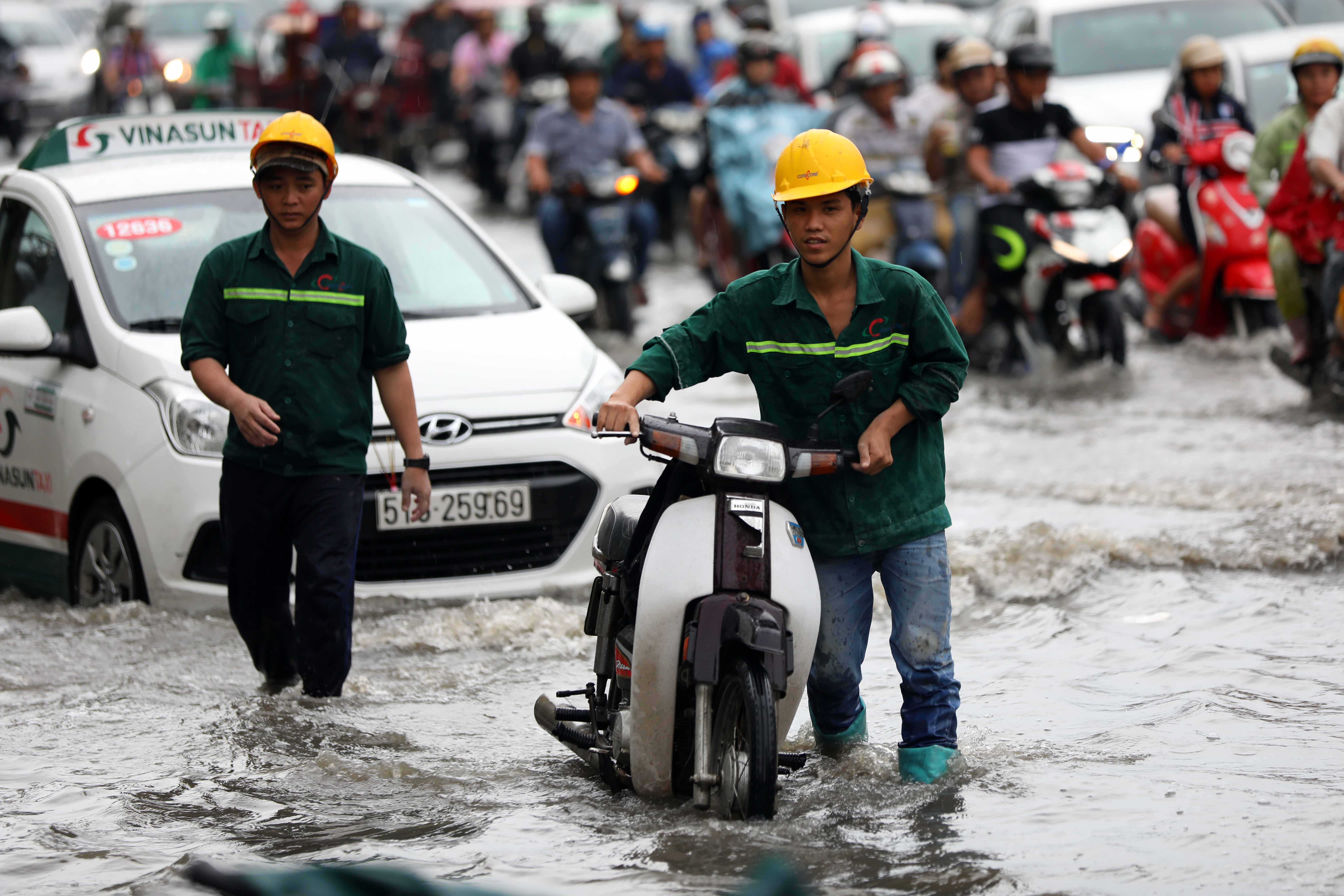 A man pushes a motorbike broken down from floodwater.