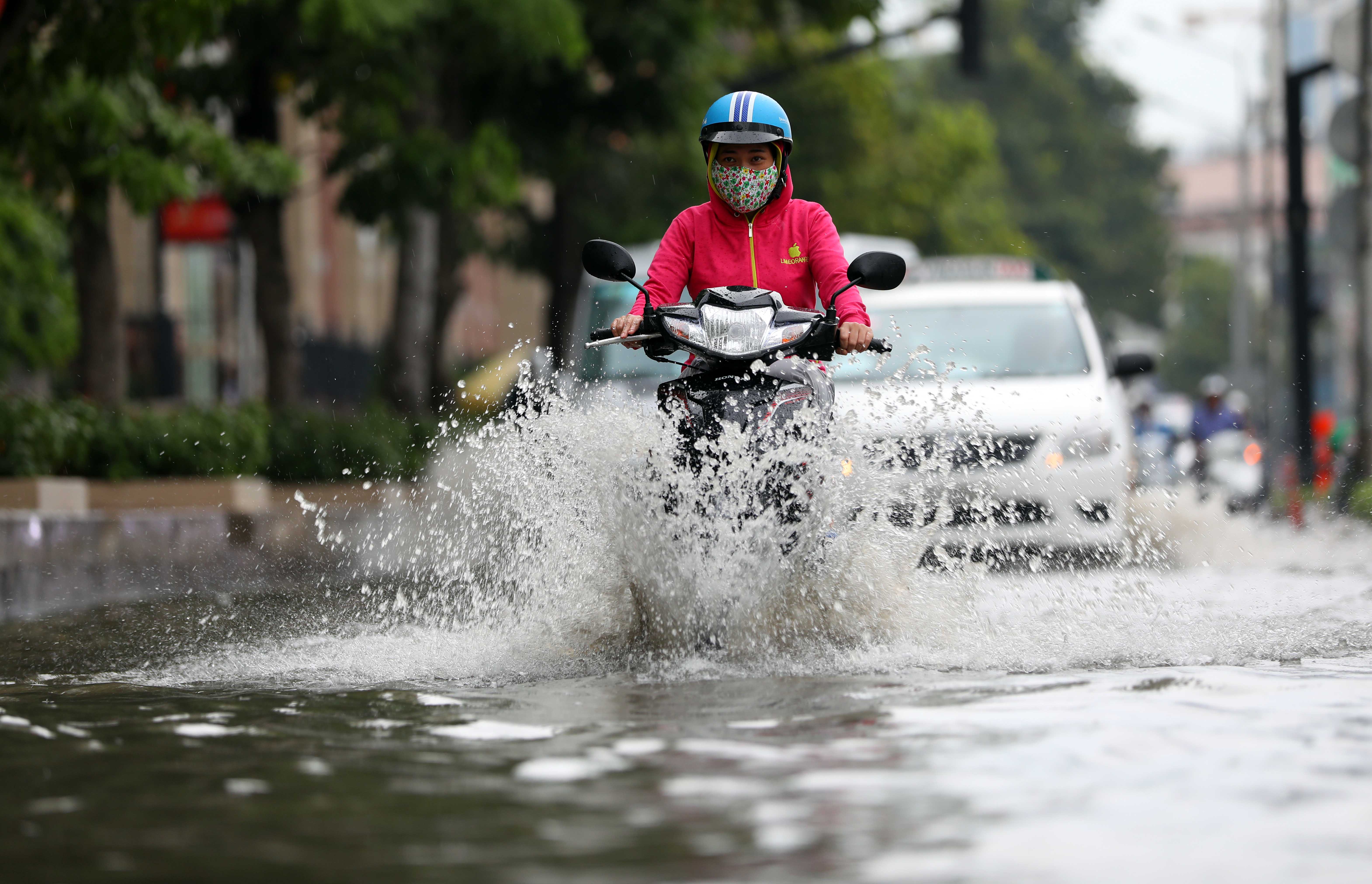 A woman rides her motorcycle through the flooded street.