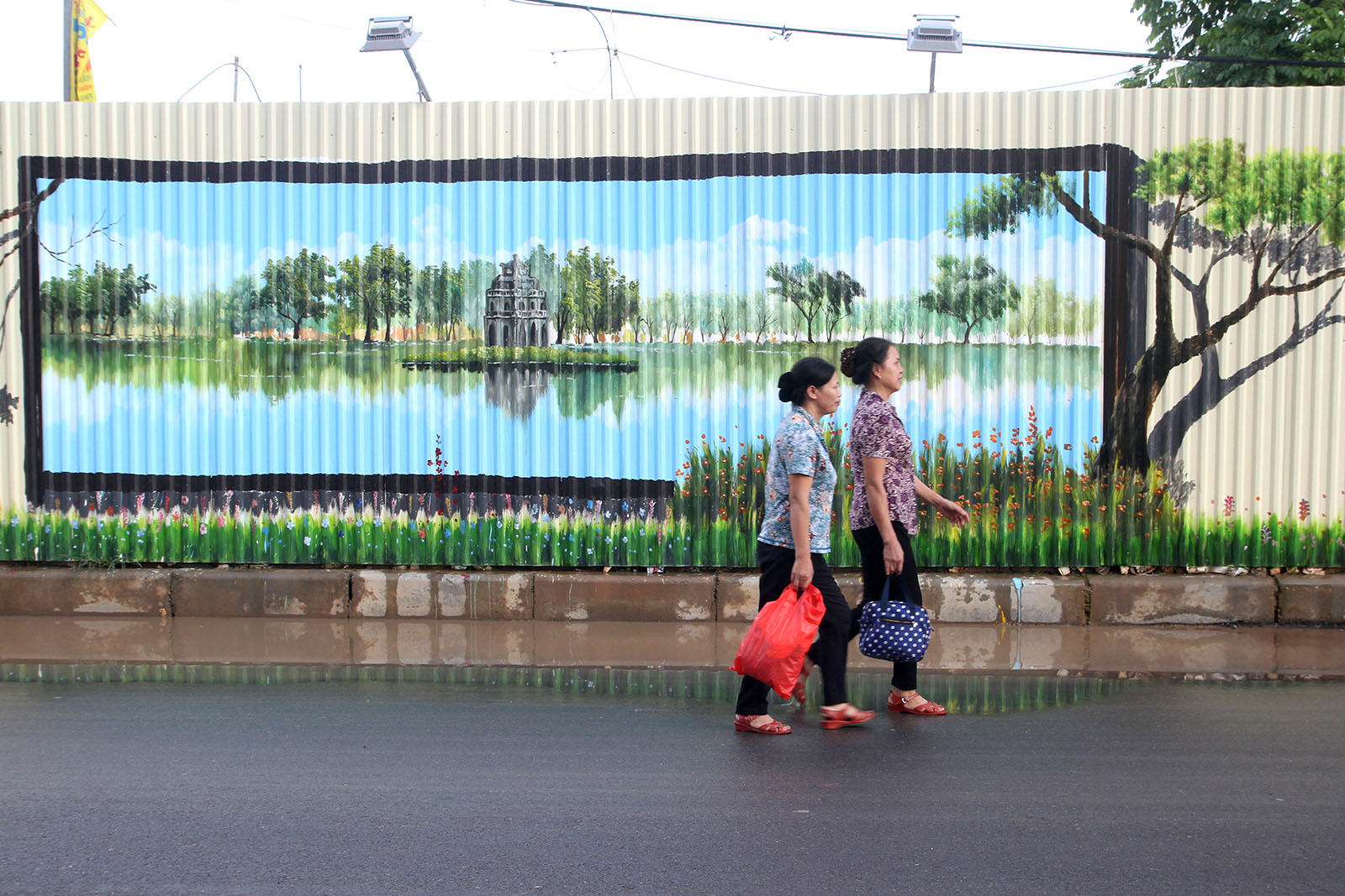 Two women walk past a painting of the Hoan Kiem Lake in Hanoi. Photo: Tuoi Tre