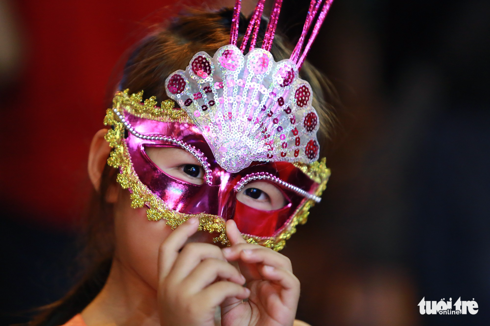 A young girl poses wearing a colorful mask.