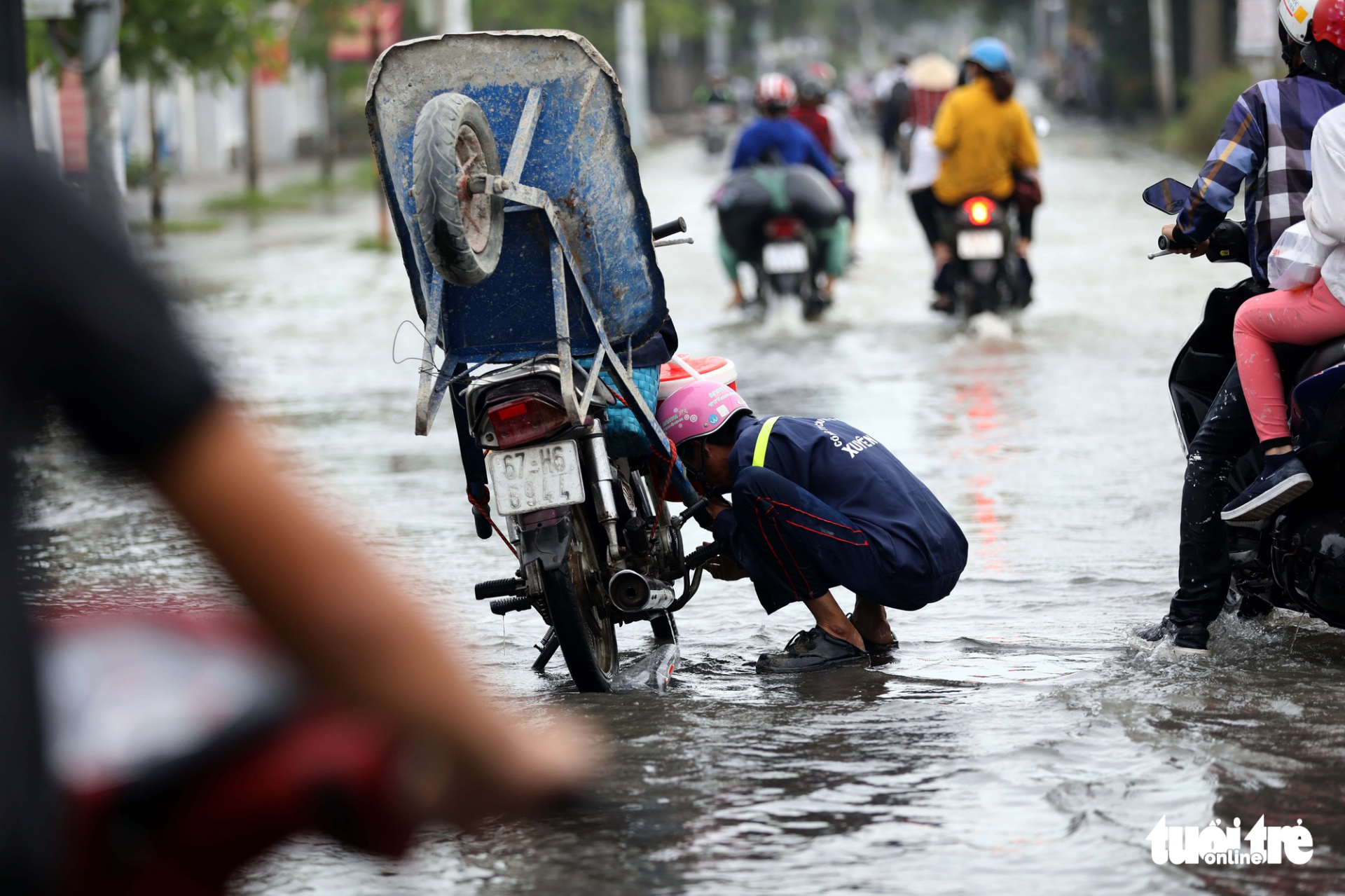 A worker tries to fix his motorbike after its engine stopped in the floodwater.