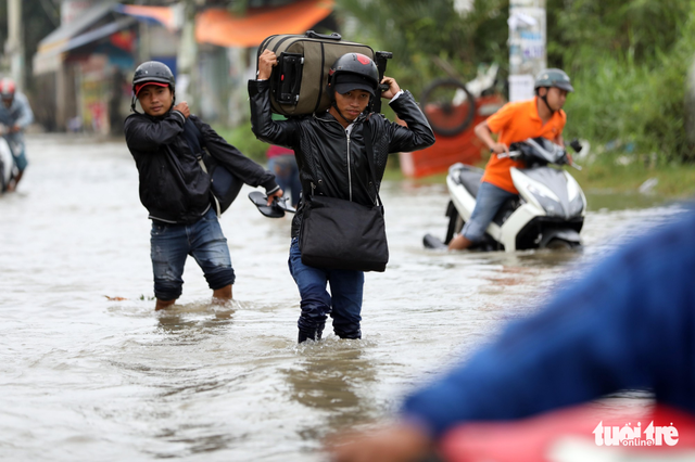 Two men carry their suitcases on the flooded street.