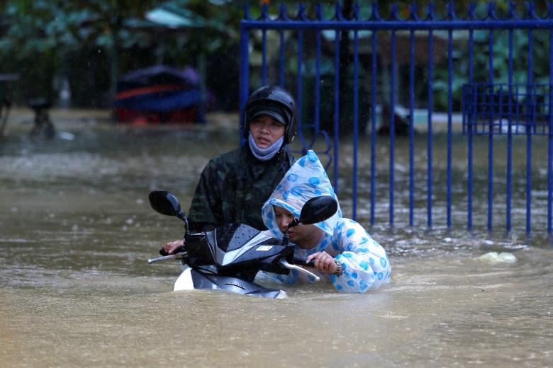 A woman pushes a motorbike along a flooded street in Hoi An. Photo: Reuters