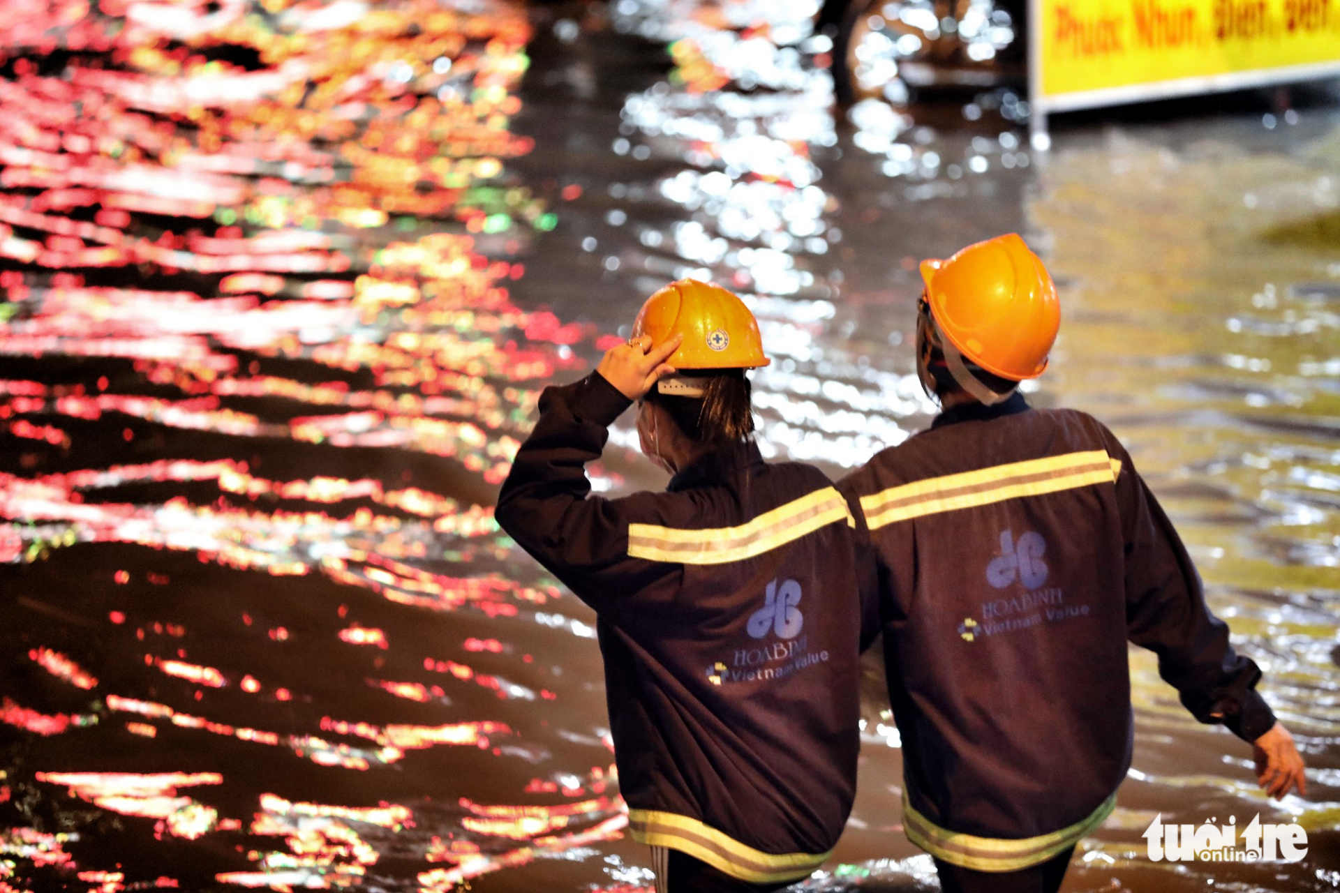 Two workers cross a flooded street. Photo: Tuoi Tre