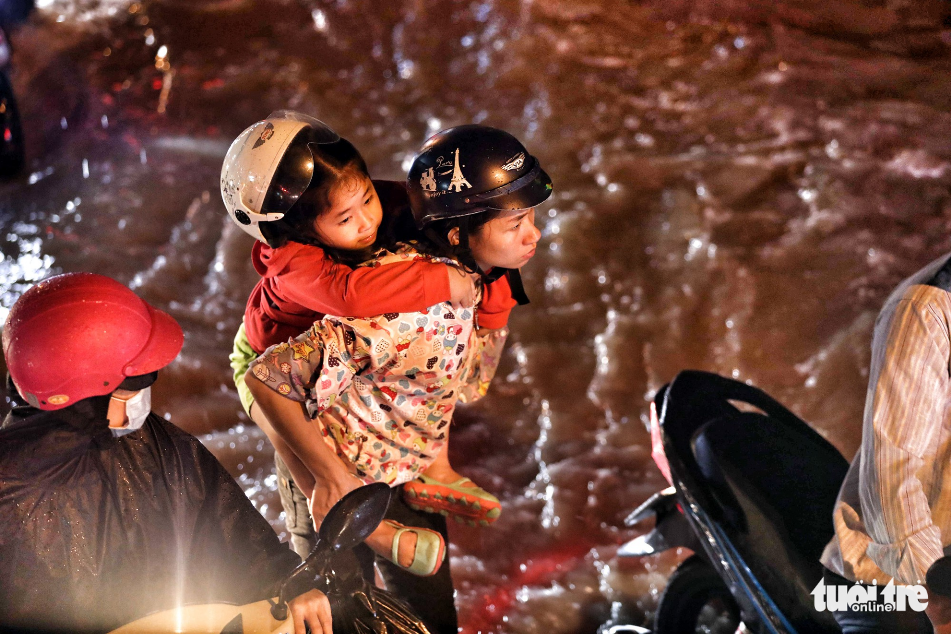 A girl is carried by her mother through a flooded street. Photo: Tuoi Tre