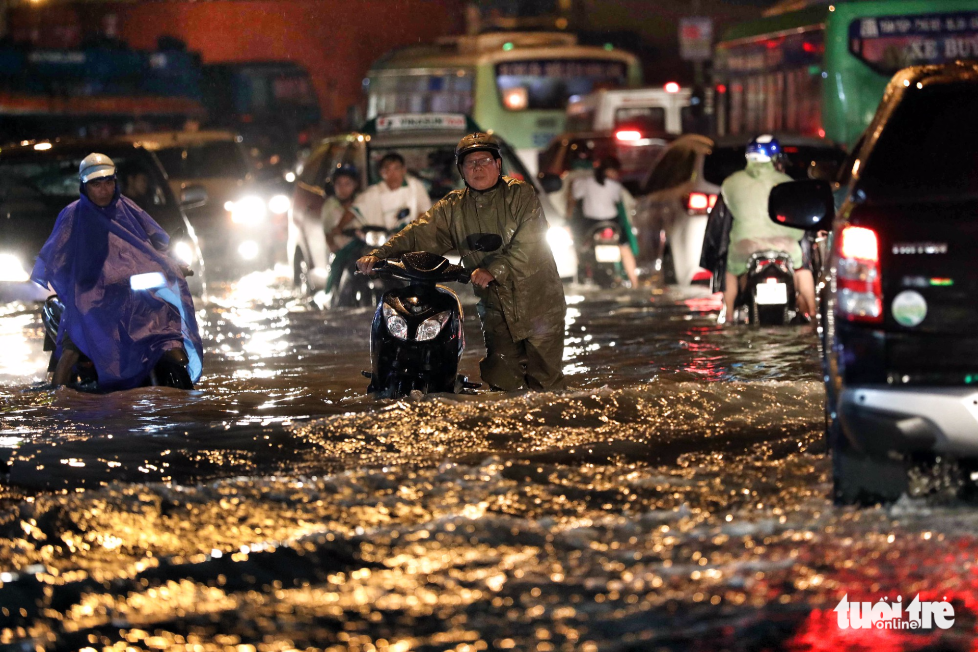Commuters push their motorbikes manually on a flooded street. Photo: Tuoi Tre