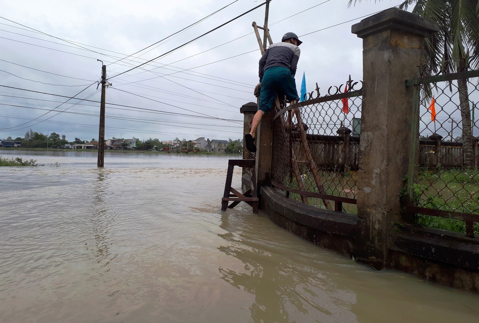 An official climbs over the fence to enter the flooded administration headquarters in Binh Tu Commune, Quang Nam Province. Photo: Tuoi Tre