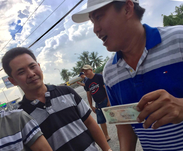 A driver (right) poses with a VND100 change he receives from the Cai Lay tollgate. Photo: Tuoi Tre