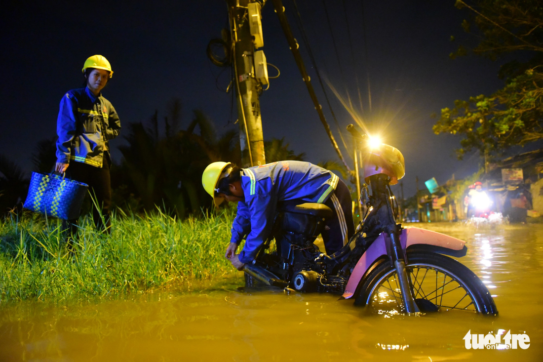 A worker fixes his motorcycle alongside the flooded street.