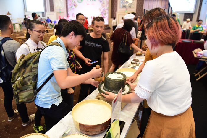 A visitor tries grinding rice into flour at the first Pho Day event in Ho Chi Minh City, December 12, 2017. Photo: Tuoi Tre