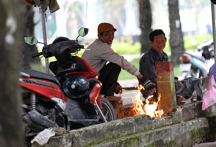 Motorbike taxi drivers sit by a bonfire in Ho Chi Minh City on December 20, 2017.