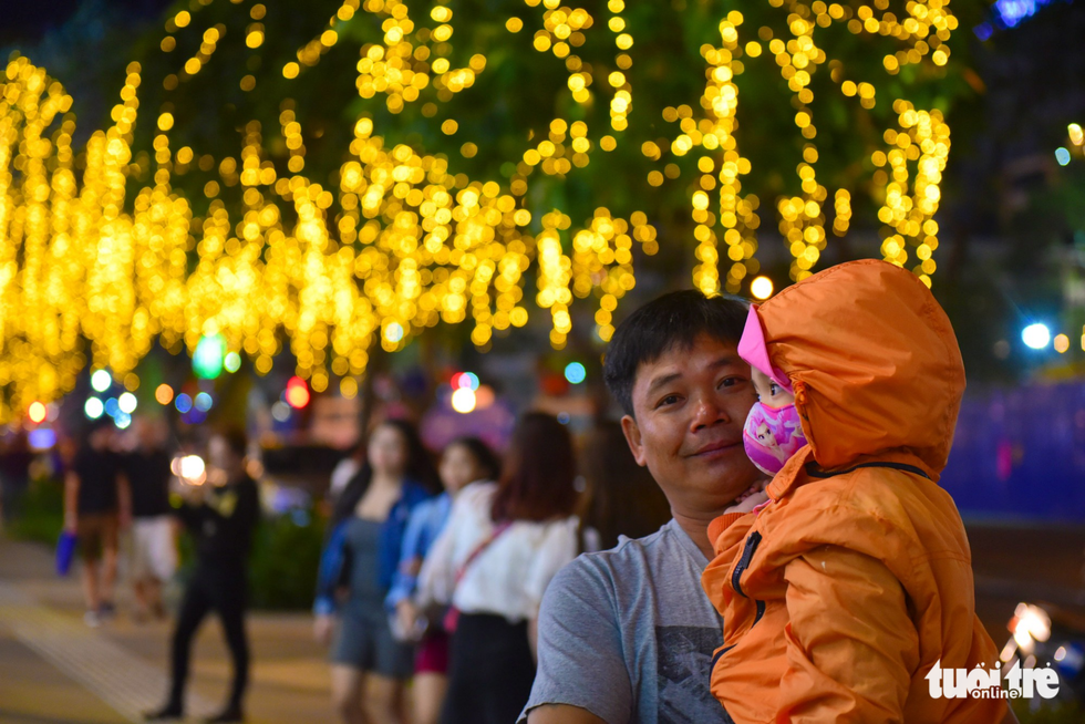 A man carries a baby while walking on a sidewalk decorated with sparkling lights in District 1, Ho Chi Minh City. Photo: Tuoi Tre