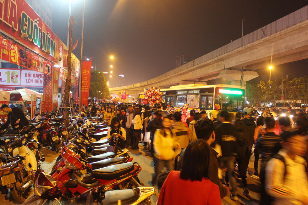 Motorbikes are parked on the sidewalk while pedestrians walk on the roadway.