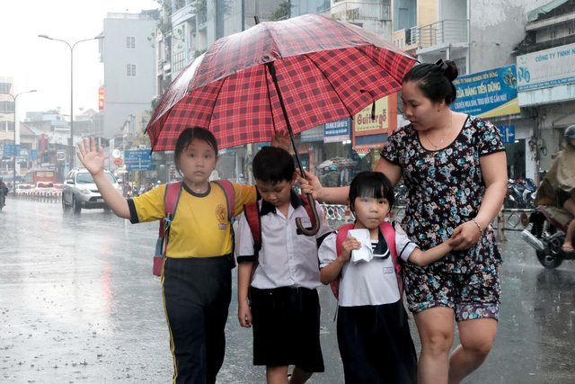 A woman protects her children from the rain with an umbrella. Photo: Tuoi Tre
