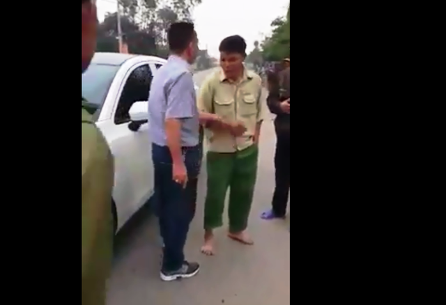 Nghia holds a gun in his right hand while talking to bystanders.