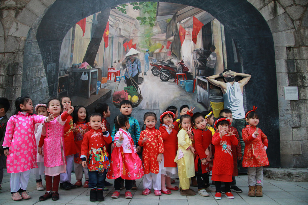 Children in red, a theme color of Tet, pose for photos with a vendor fresco in the background. Photo: Tuoi Tre
