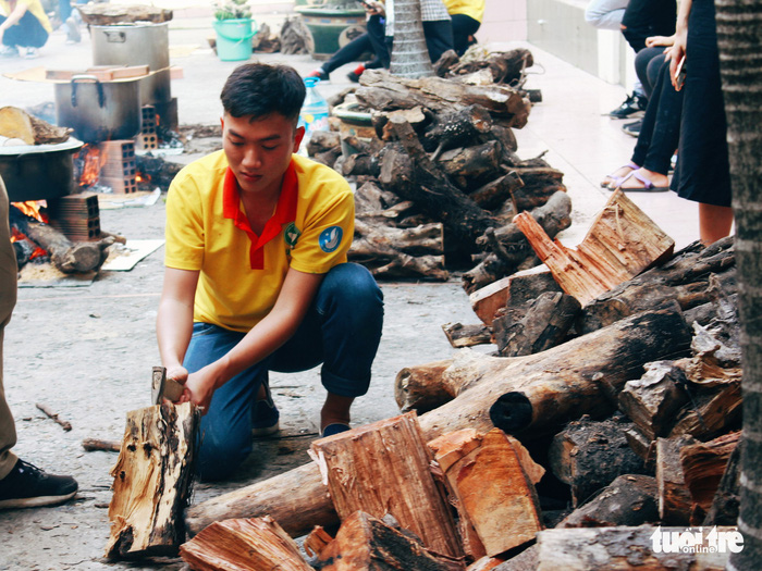 A volunteer chops wood to boil water for steaming the cakes. Photo: Tuoi Tre