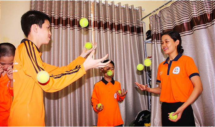 Autistic children (L) juggle tennis balls with instructions from a trainer (R). Photo: Tuoi Tre