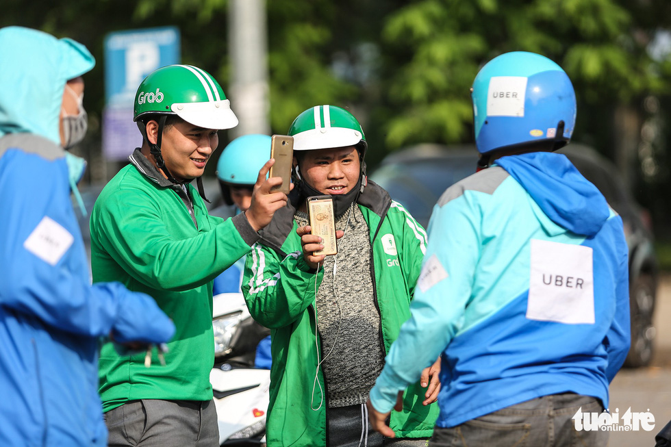 Two Grab drivers (wearing green uniforms) film the parade staged by Uber drivers in Hanoi on the last day of the company’s operation in Vietnam, April 8, 2018. Photo: Tuoi Tre