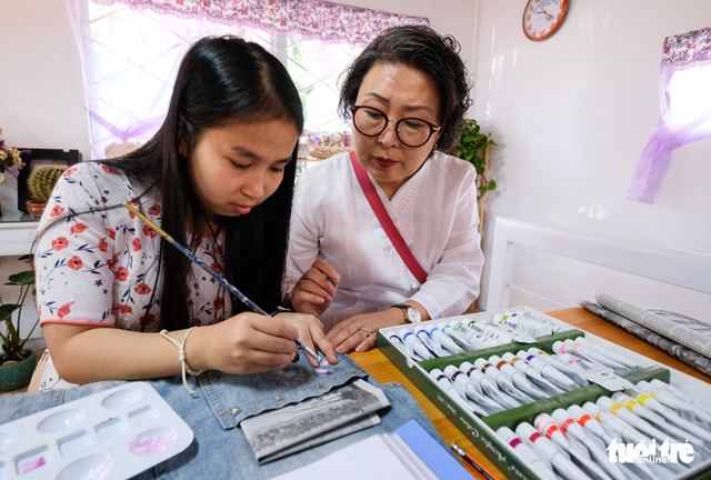 A voluntary South Korean woman helps a Vietnamese student with hearing loss draw decorations on a piece of clothing at the Lam Dong School for the Deaf in Lam Dong Province, Vietnam. Photo: Tuoi Tre