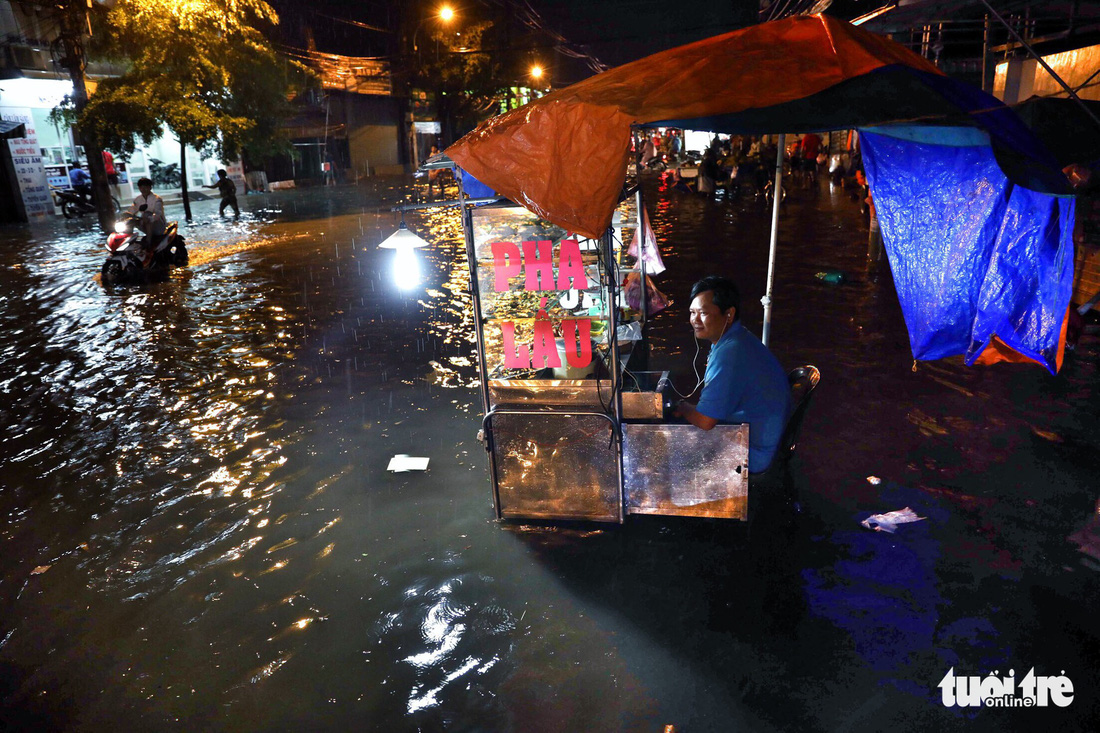 A food vendor sits among the floodwater on Ho Ngoc Lam Street in Binh Tan District.