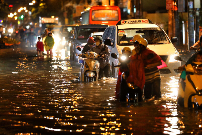 People walk their motorcycles along submerged Ho Hoc Lam Street in Ho Chi Minh City, on May 19, 2018. Photo: Tuoi Tre