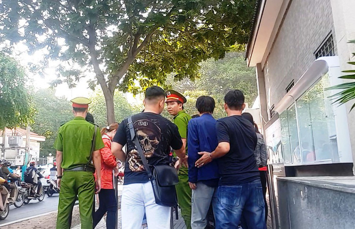 An intermediary (R) helps a client cut the line despite the presence of police officers. Photo: Tuoi Tre