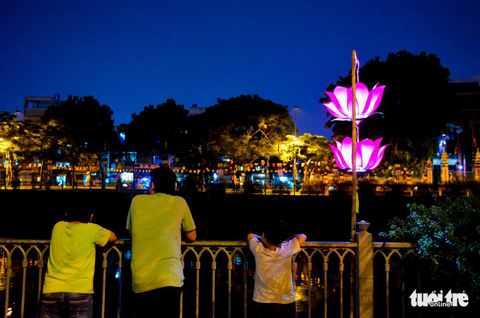 A man together with his two sons watches the lanterns and the giant lotus shining on the canal. Photo: Tuoi Tre