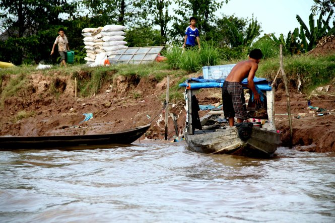 A man anchors his boat at an eroded river bank in An Giang Province, Vietnam. Photo: Tuoi Tre