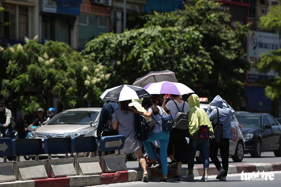 A group of residents cover themselves with jackets and umbrellas as they cross Tay Son Street in Hanoi.