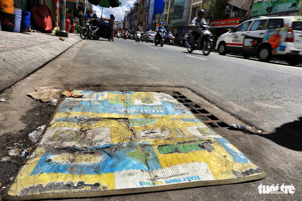 Locals cover up a manhole to block the smell on Phan Dinh Phung Street in Phu Nhuan District.