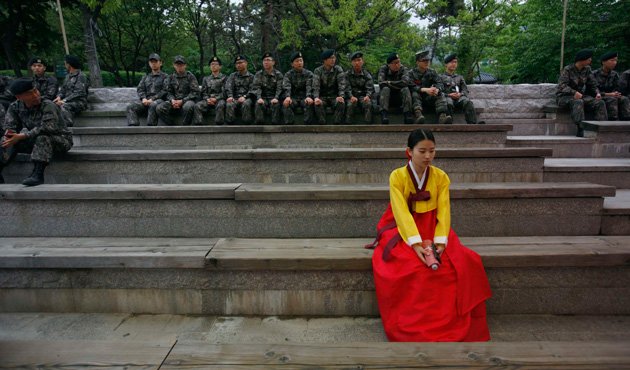 A woman wearing a traditional Korean Hanbok costume sits in front of South Korean soldiers before a traditional coming-of-age day ceremony at Namsangol Hanok Village in Seoul May 20, 2013.