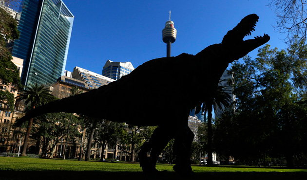 A performer dressed in a Tyrannosaurus rex dinosaur costume is silhouetted in front of buildings during a publicity event in central Sydney August 28, 2013.