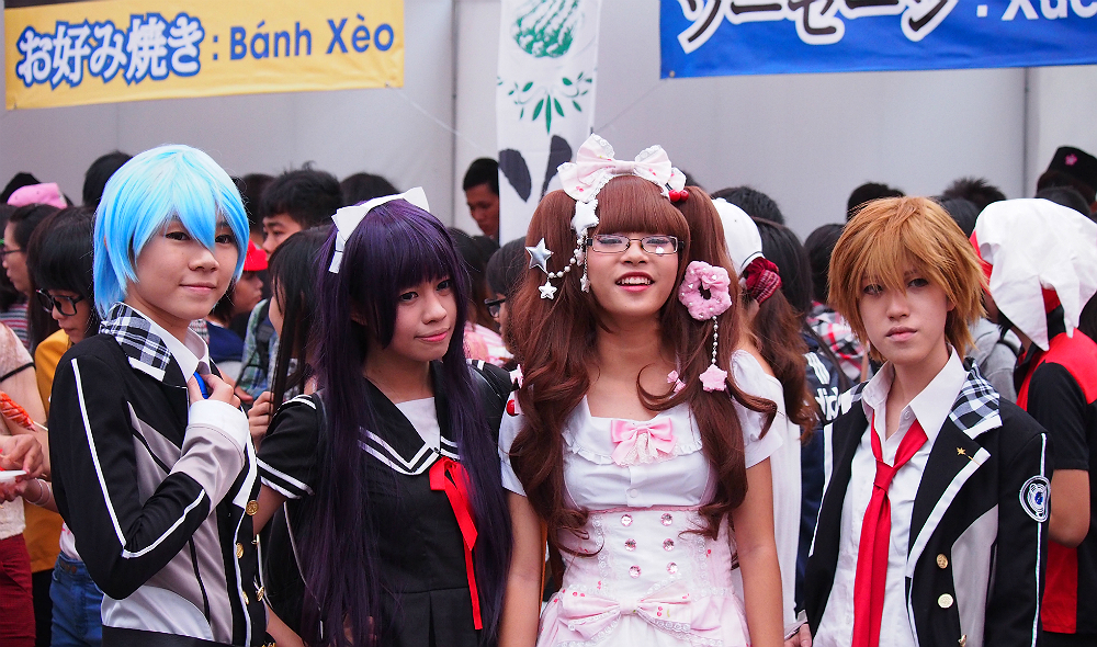 A cosplay group poses for a group photo in front of Japanese food stalls.