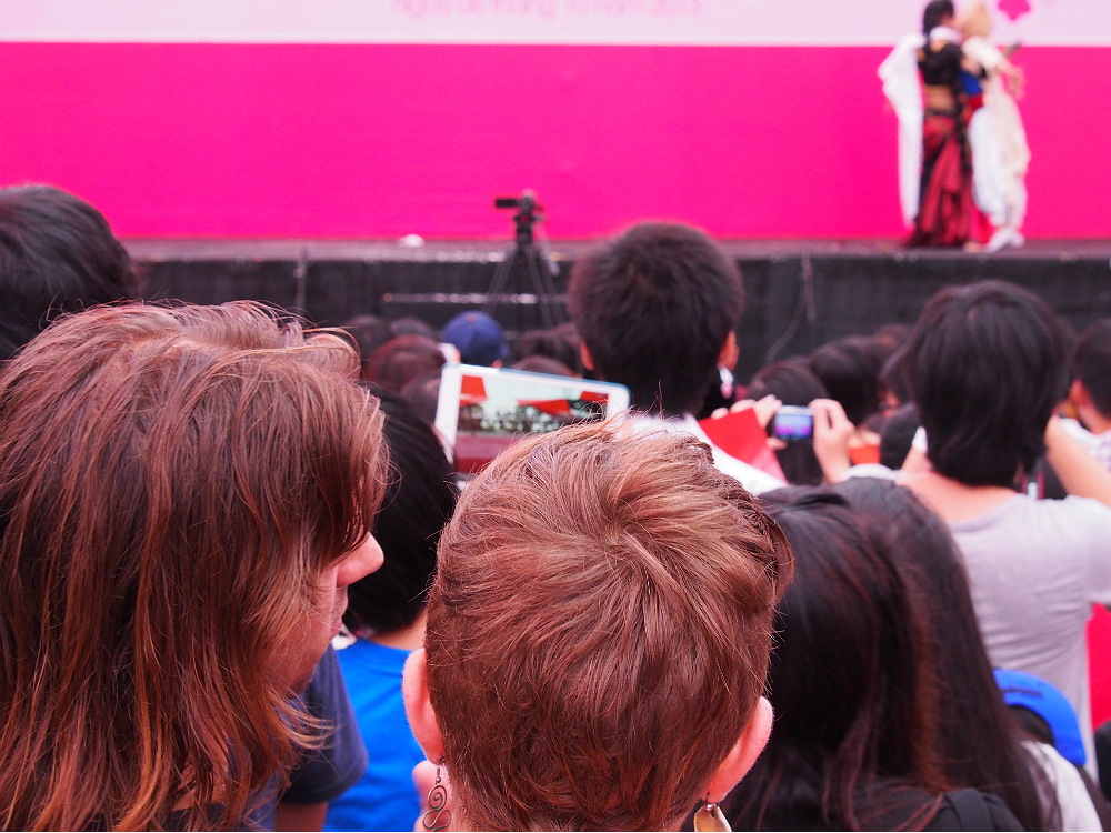 A foreign couple watches a cosplay show on stage.