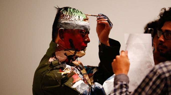 Liu Bolin, a Chinese artist, applies paint to his forehead as he prepares to blend himself into a backdrop, a shelf lined with comic books, as part of a series of performances in Caracas, November 2, 2013.