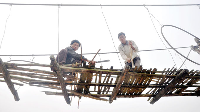 Lo Van Dam (L), leader of Khon Doi hamlet, and another local man repair a suspension bridge in his locality. Dam said local people have asked authorities to build a new bridge for the last three years but no bridge has been built up to now.