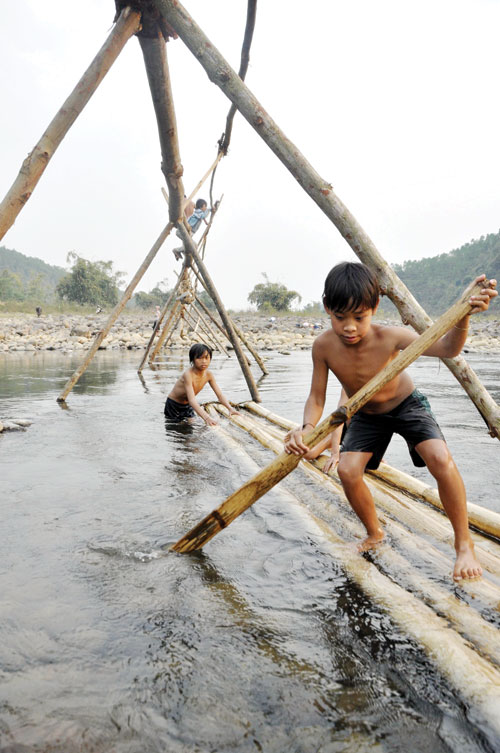 Two boys row a raft. Residents in Lai Chau annually build rafts to prepare for the flooding season when bridges are swept away by floodwater.