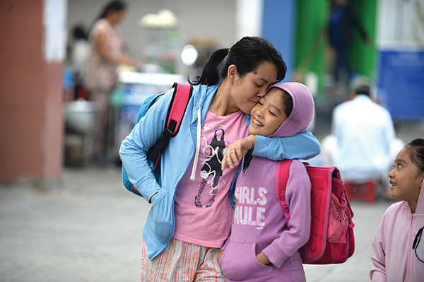 A mother kisses her daughter, both wearing hoodies, on the way to the kid's school on Nguyen Thai Son Street in Go Vap District. 