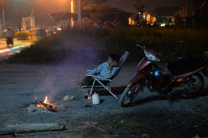 Nguyen Van Lam, a seasoned “xe om” (motorbike taxi) driver on District 8’s Nguyen Van Linh street builds a fire while seeking customers.