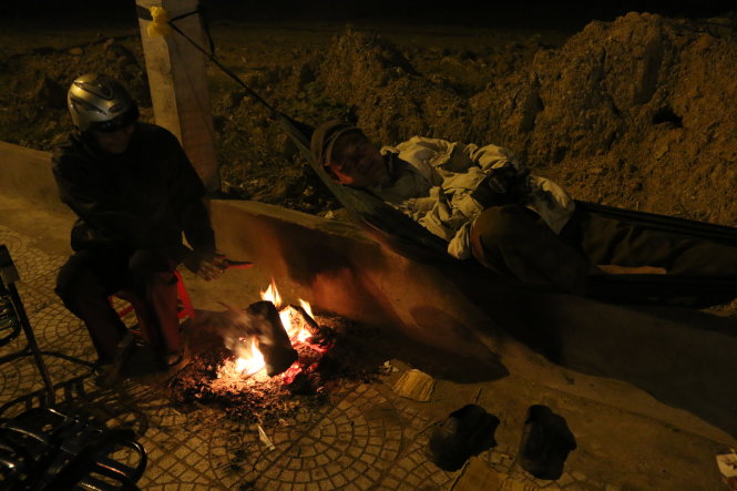 A laborer is seen taking rest over the warmth of a fire near by.