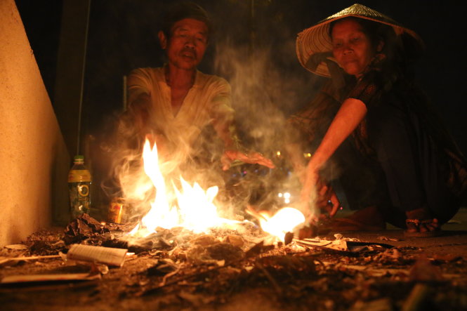 A middle-aged couple relish in the warmth of a fire while waiting for dawn to break to begin their day's work.