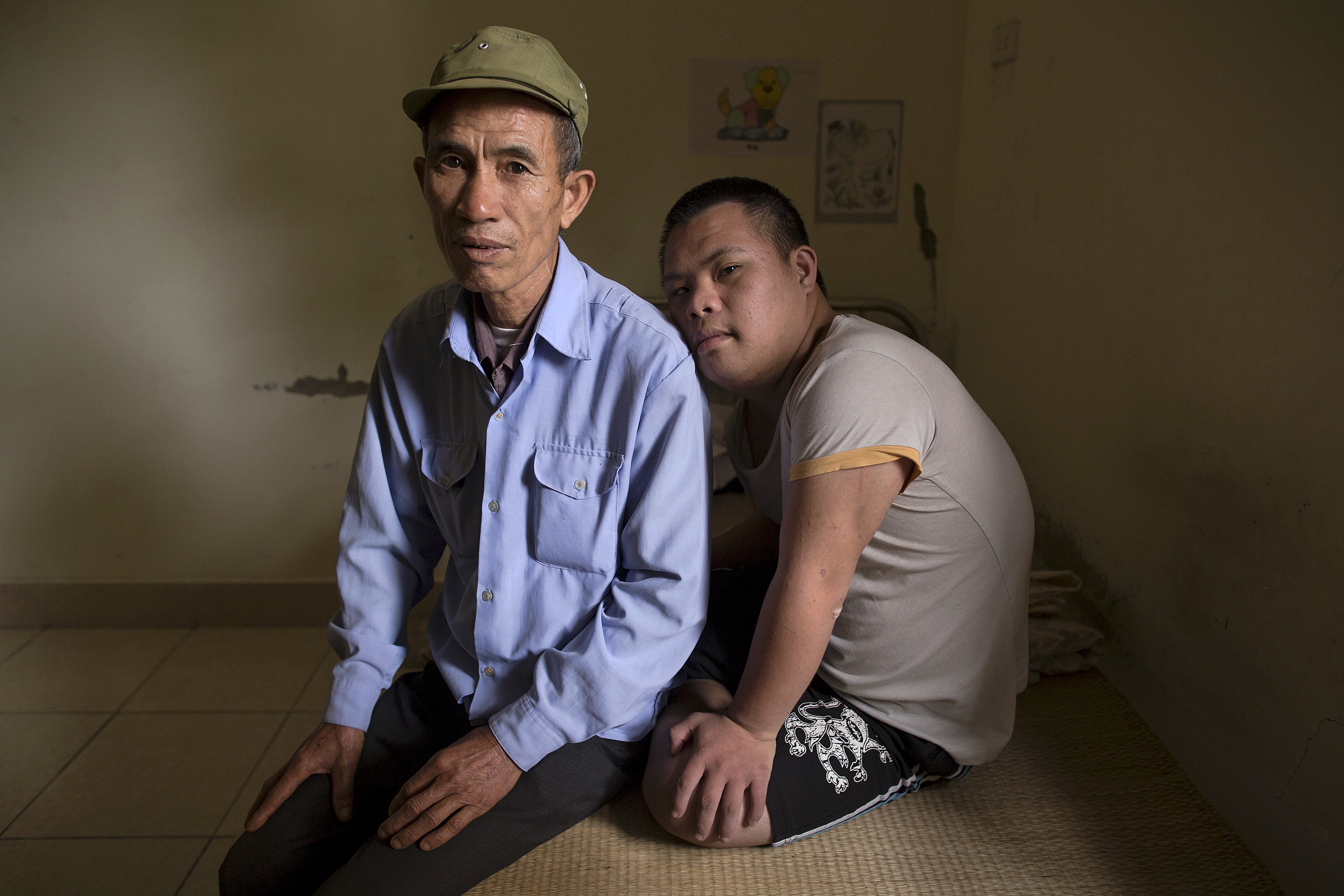 3-year-old former soldier, Nguyen Hong Phuc, sits on the bed with his son Nguyen Dinh Loc, 20, who is recovering from tumour surgery at Friendship village, a hospice for Agent Orange victims, outside Hanoi April 8, 2015. Nguyen Dinh Loc has serious mental and physical problems that his family and doctors link to his father's exposure to Agent Orange. His father joined the military after the U.S. army stopped using Agent Orange in 1971, but lived in areas heavily contaminated by it, including near Danang airport, where the chemical defoliant was stored.