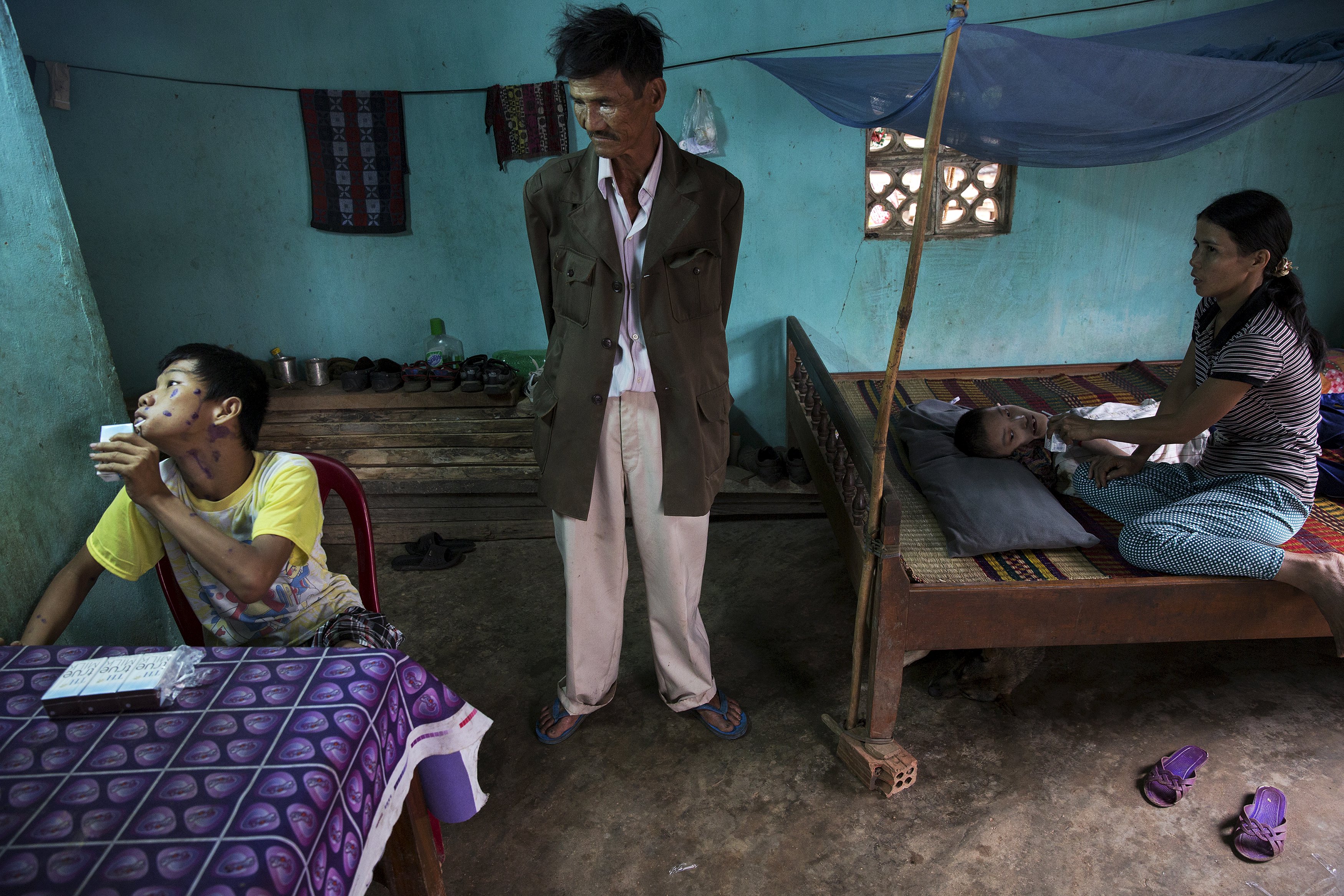 Le Van Dan (C) looks at his disabled grandson Le Van Tam (L) as his daughter feeds another sick grandson in their family house in Phuoc Thai village, outside Danang April 12, 2015. Le Van Dan, a former artillery soldier, said he was exposed to Agent Orange more than once, including being directly sprayed by U.S. planes near his village before he joined the military. Health officials confirmed two of his grandsons’ disabilities are due to his exposure to the defoliant, Le Van Dan said.