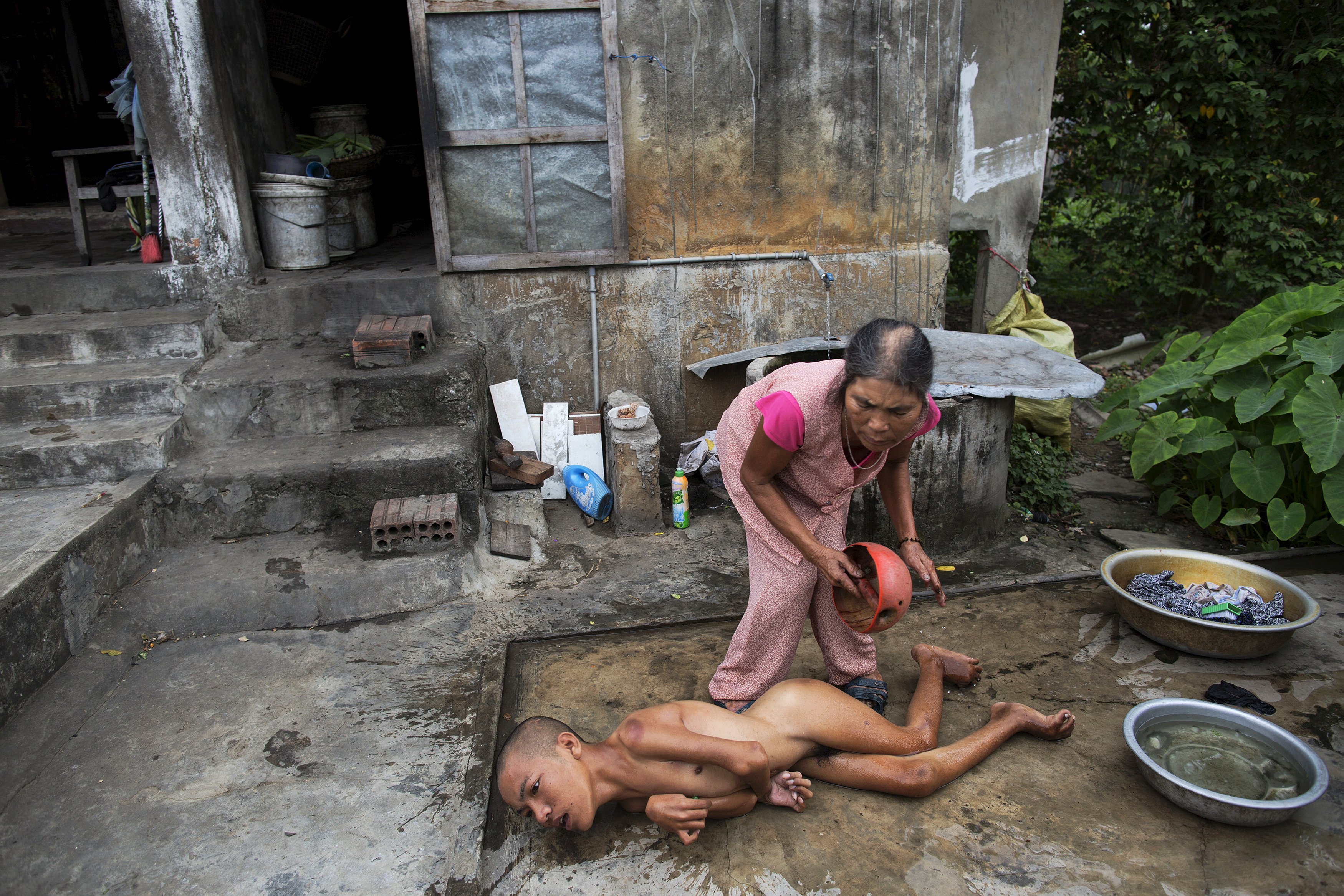 Tang Thi Thang baths her disabled son Doan Van Quy outside their family home in Truc Ly, in Vietnam's Quang Binh Province April 11, 2015. Doan Van Quy's father, a soldier who served on 12.7 mm anti-aircraft guns during the Vietnam War, said he lived in several areas that were contaminated by Agent Orange. Two of his sons were born with serious health problems and the family and local health officials link their illnesses to their father's exposure to Agent Orange.