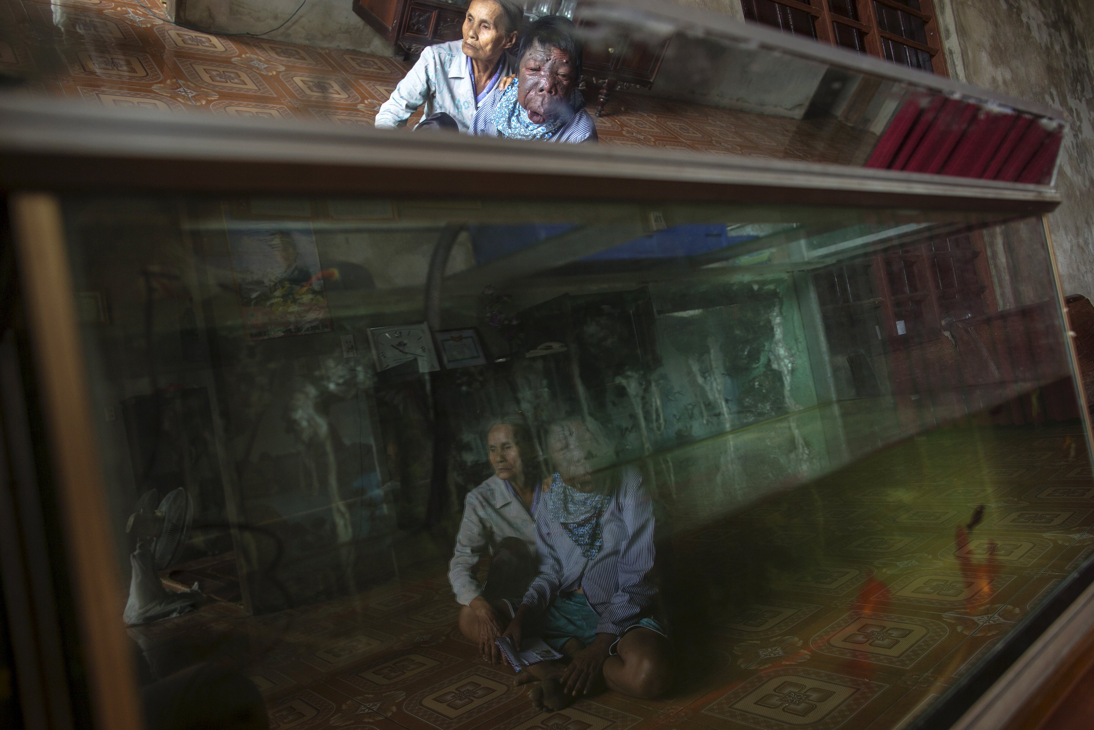 Dang Thi Quang and her son Nguyen Van Binh are reflected in an aquarium in their home in Vietnam's Quang Binh province April 11, 2015. Nguyen Van Binh’s father, a soldier who served in the Vietnamese army's transportation unit in the North, travelled and spent time in areas known as hotspots for Agent Orange contamination.