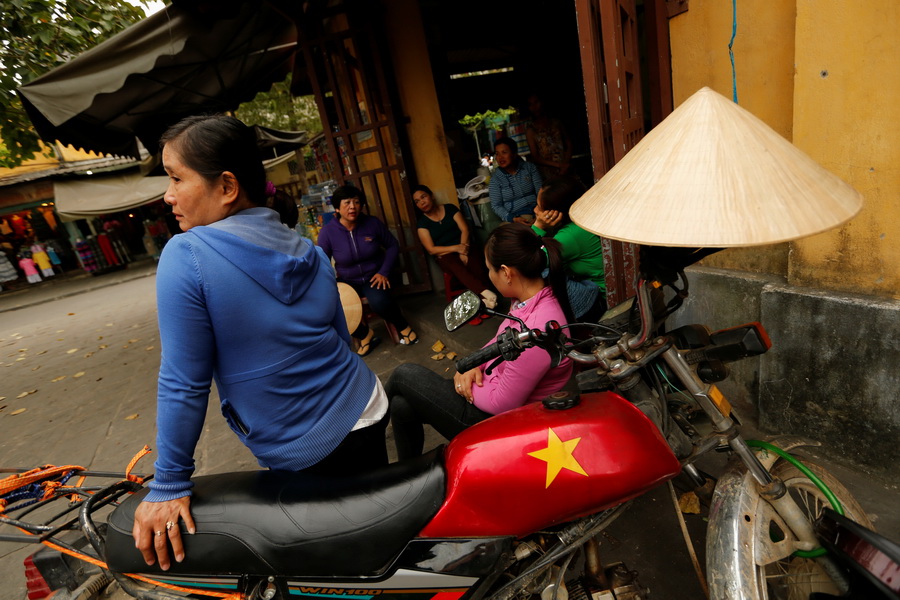 A woman sits on a motorcycle outside a market in Hoi An, Vietnam April 4, 2016.